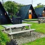 A luxurious site glamping in Derry, Northern Ireland, featuring a cozy pod, hot tub, fire pit, and lush greenery