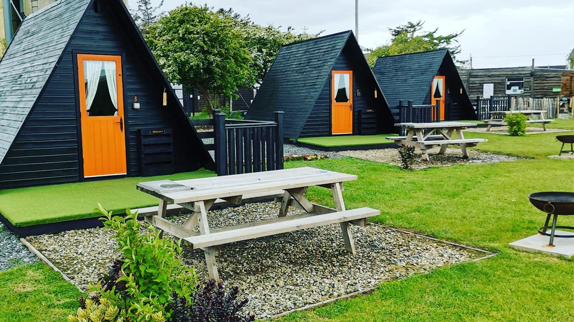 A luxurious site glamping in Derry, Northern Ireland, featuring a cozy pod, hot tub, fire pit, and lush greenery